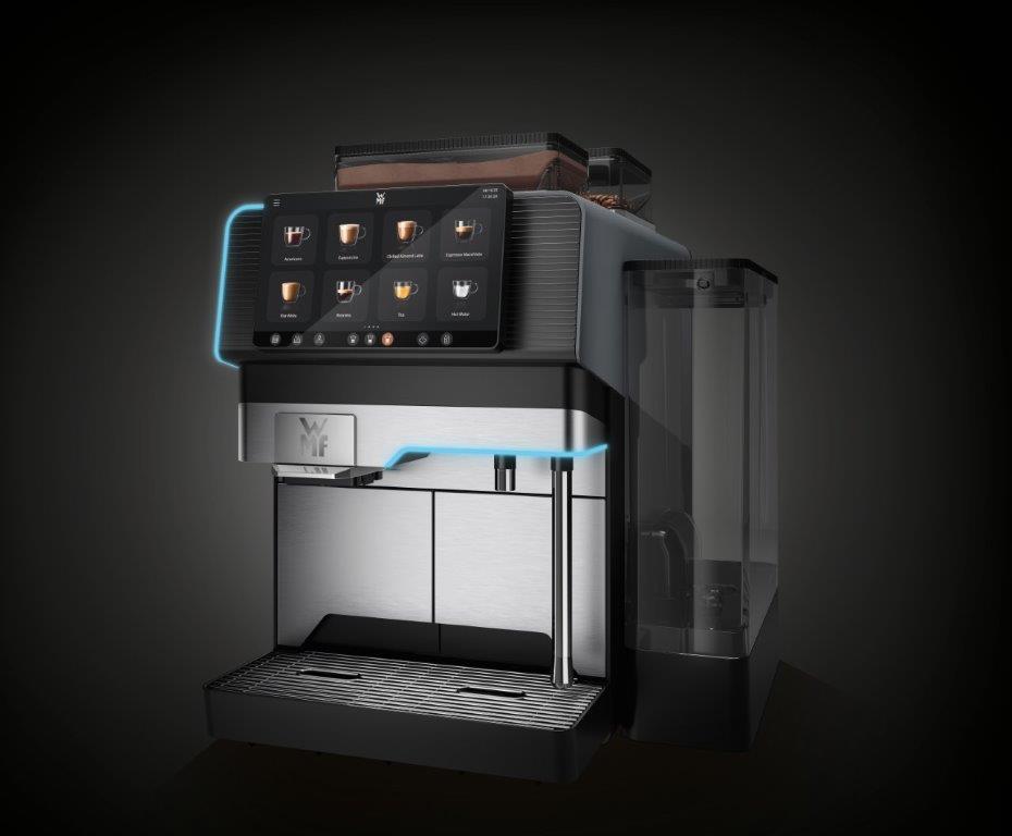 Na zdjęciu zaprezentowano ekspres WMF Elevation 10 w eleganckim ujęciu perspektywicznym. Widoczny jest duży ekran dotykowy z menu napojów, pojemnik na wodę oraz pojemniki na kawę i proszki. Nowoczesny design z niebieskim podświetleniem podkreśla charakter premium urządzenia, które idealnie sprawdza się w biurach, hotelach i salonach, oferując do 50 filiżanek napojów dziennie w jakości baristycznej.